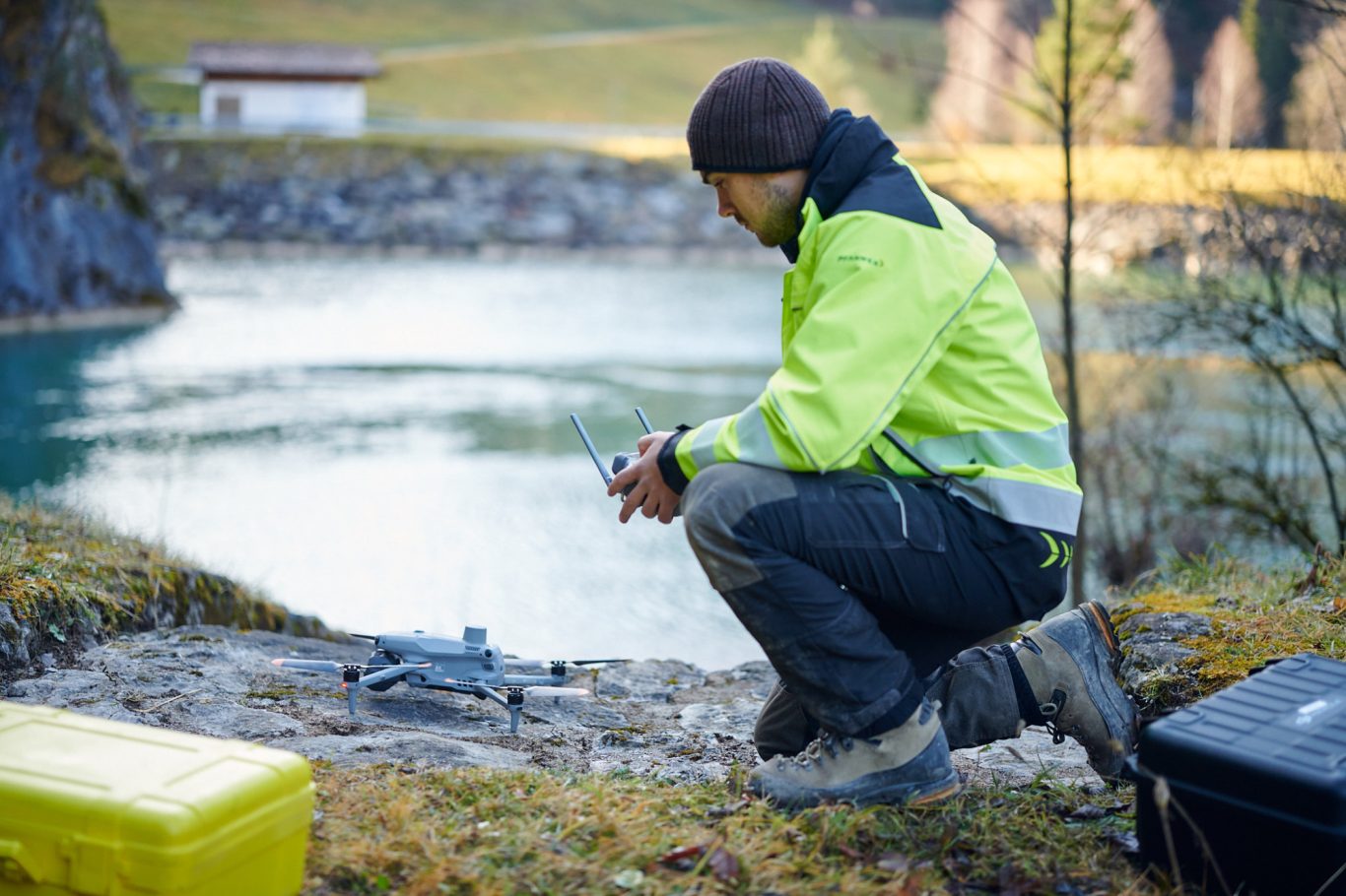 UAV Vermessung vor Ort Arbeiter in Sicherheitskleidung kniet am Wasser und kontrolliert ein Gerät.